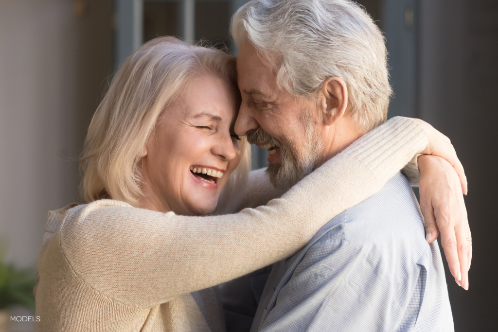 middle-aged woman and man with their arms around each other, smiling and laughing, foreheads together