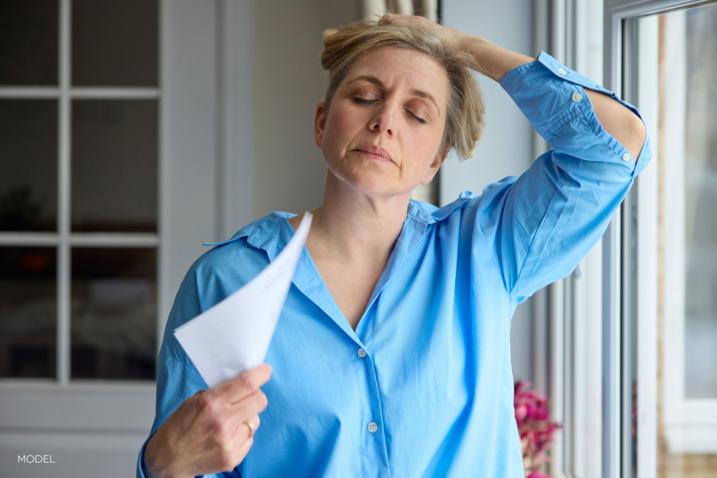 menopausal woman having a hot flash, holding hair up and fanning face with a piece of paper