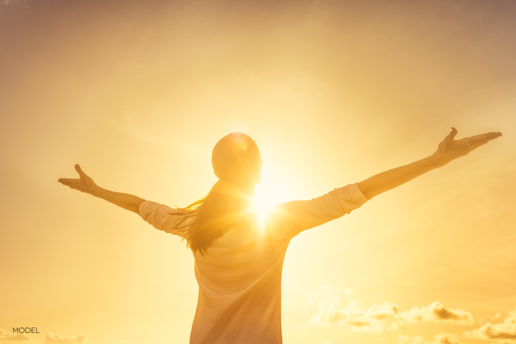 woman backlit by sunset, bright yellow colors, with her arms outstretched