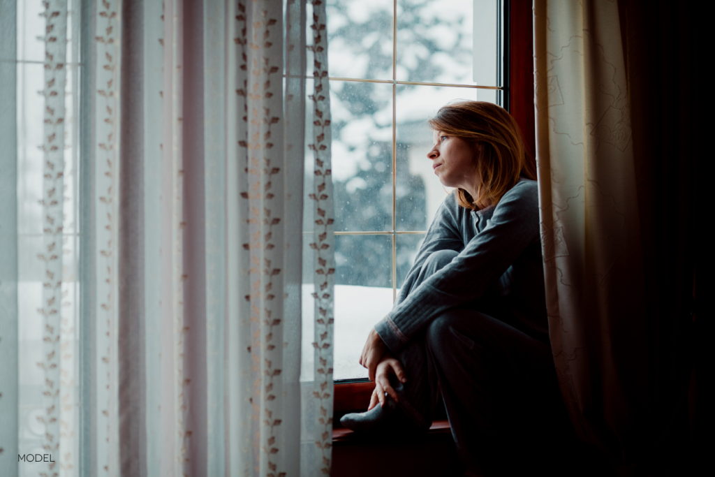 woman looking out the window at the snow with a serious, thoughtful expression