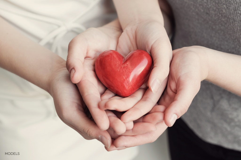 hands holding a heart shaped red rock
