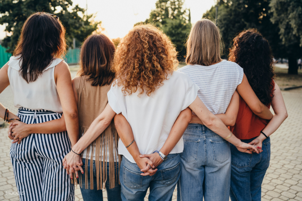 image of group of women from behind, arms around each other and linked by their hands