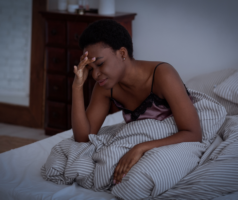 Woman in bed, sitting up and holding her head due to headache or migraine